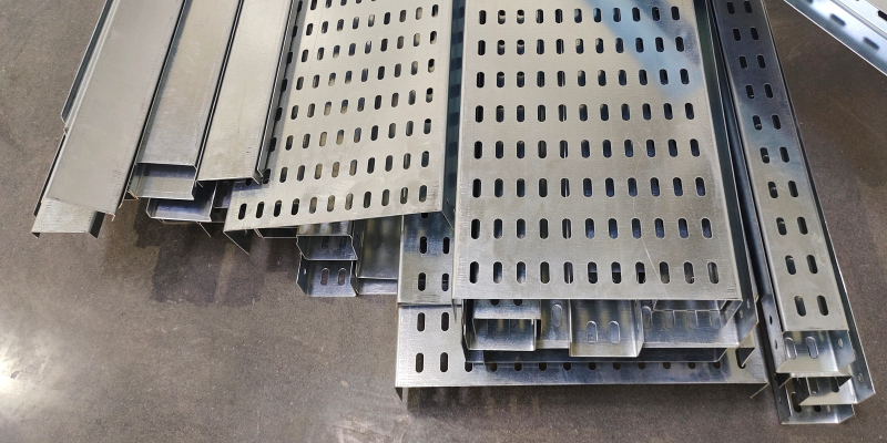 Galvanised iron slotted cable trays of various types and sizes stacked on concrete floor.